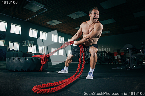 Image of Shirtless man flipping heavy tire at gym