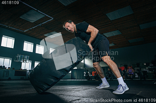 Image of Shirtless man flipping heavy tire at gym