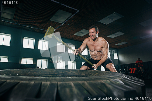 Image of Shirtless man flipping heavy tire at gym