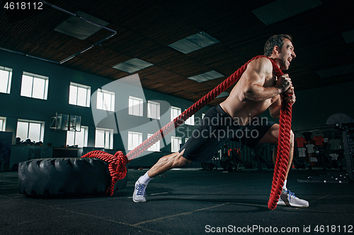 Image of Shirtless man flipping heavy tire at gym