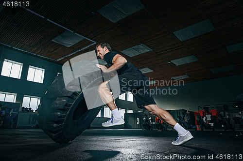 Image of Shirtless man flipping heavy tire at gym