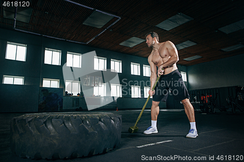 Image of Shirtless man flipping heavy tire at gym