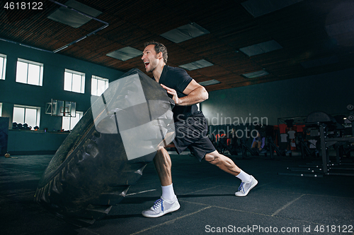 Image of Shirtless man flipping heavy tire at gym