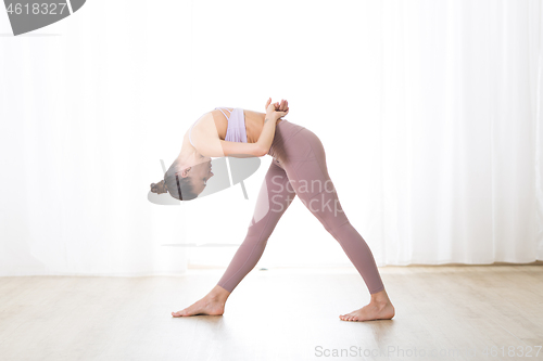 Image of Portrait of gorgeous active sporty young woman practicing yoga in studio. Beautiful girl practice Dandayamana Bibhaktapada Jauushirasana, standing separate leg head to knee pose