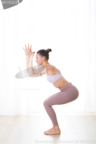 Image of Portrait of gorgeous active sporty young woman practicing yoga in studio. Beautiful girl practice Garurasana, eagle yoga pose. Healthy active lifestyle, working out indoors in gym