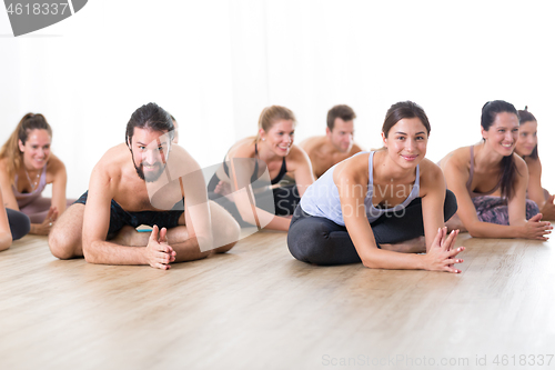 Image of Group of young sporty attractive people in yoga studio, practicing yoga lesson with instructor, sitting on floor in forward band stretching yoga pose. Healthy active lifestyle, working out in gym