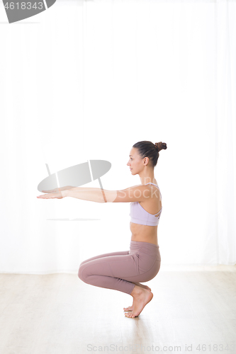 Image of Portrait of gorgeous active sporty young woman practicing yoga in studio. Beautiful girl practice Utkatasana, awkward yoga pose. Healthy active lifestyle, working out in gym