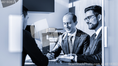 Image of Group of confident successful business people reviewing and signing a contract to seal the deal at business meeting in modern corporate office.