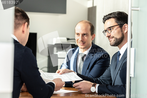 Image of Group of confident successful business people reviewing and signing a contract to seal the deal at business meeting in modern corporate office.