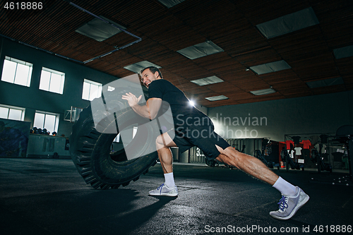 Image of Shirtless man flipping heavy tire at gym