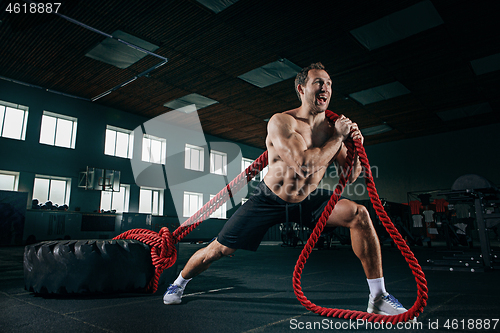 Image of Shirtless man flipping heavy tire at gym