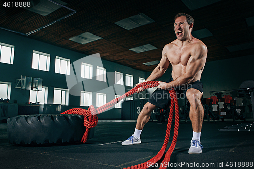 Image of Shirtless man flipping heavy tire at gym