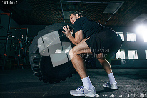 Image of Shirtless man flipping heavy tire at gym