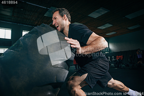 Image of Shirtless man flipping heavy tire at gym