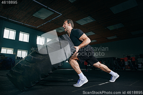 Image of Shirtless man flipping heavy tire at gym