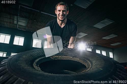 Image of Shirtless man flipping heavy tire at gym