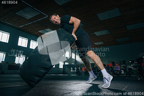 Image of Shirtless man flipping heavy tire at gym