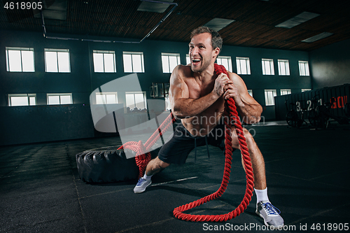 Image of Shirtless man flipping heavy tire at gym