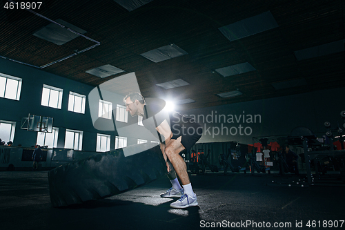 Image of Shirtless man flipping heavy tire at gym