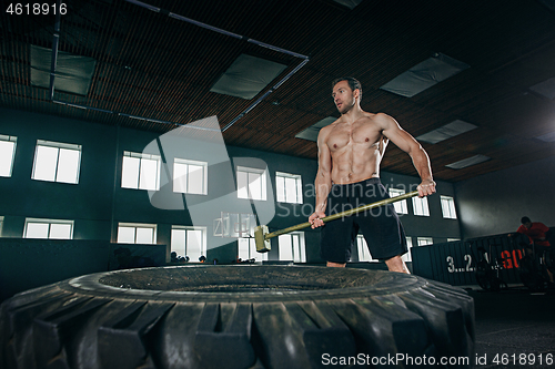 Image of Shirtless man flipping heavy tire at gym