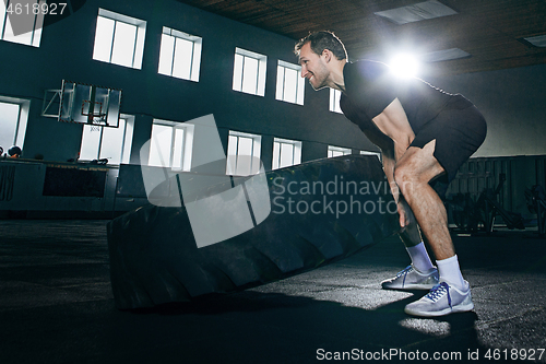 Image of Shirtless man flipping heavy tire at gym