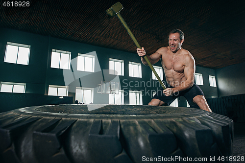 Image of Shirtless man flipping heavy tire at gym