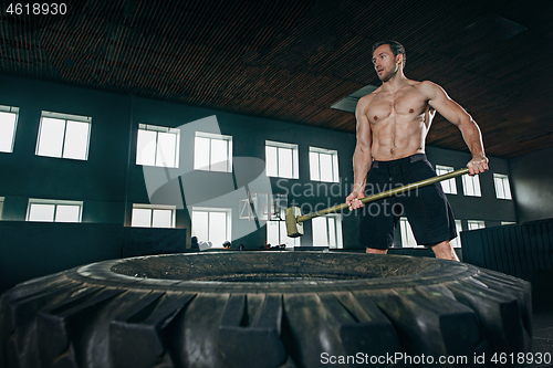 Image of Shirtless man flipping heavy tire at gym