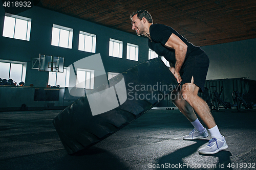 Image of Shirtless man flipping heavy tire at gym