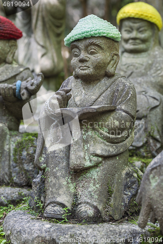 Image of Old stone statue of Buddhist monk wearing knitted hat with book in his hands.