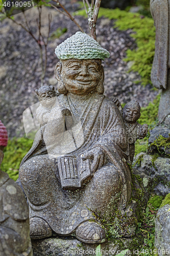 Image of Old stone statue of Buddhist monk wearing knitted hat with book in his hands.