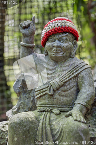 Image of Old stone statue of Buddhist monk wearing knitted hat pointing the finger up.