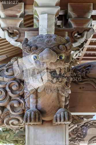 Image of Wooden carving of an angry Komainu decorates the gable of a roof over the entrance of an ancient Buddhist temple in Japan.