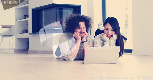 Image of young multiethnic couple using a laptop on the floor