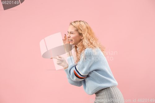 Image of The young woman whispering a secret behind her hand over pink background