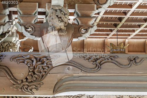 Image of Wooden carving of an angry Komainu decorates the gable of a roof over the entrance of an ancient Buddhist temple in Japan.