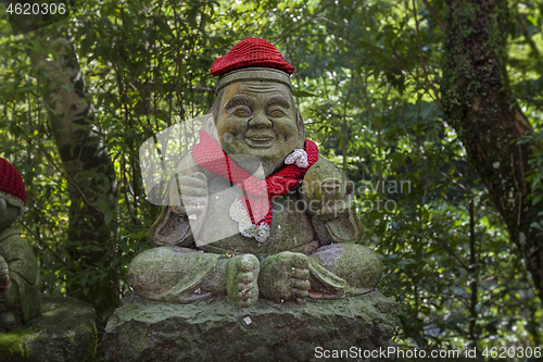 Image of Old stone statue of Buddhist monk wearing knitted hat with fish in his hands.