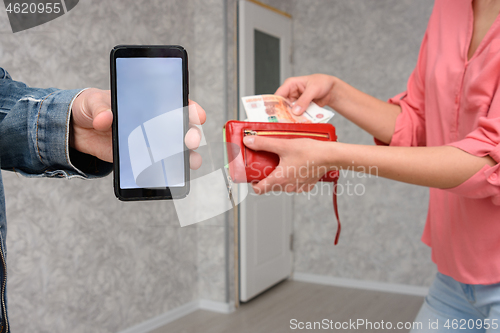 Image of A man shows a mobile phone screen close-up, a girl takes out cash from a purse for paying for a room repair service