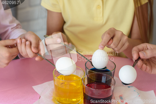 Image of Hands dip chicken eggs in a dye solution