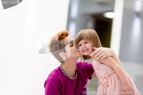 Image of young mother helping daughter while putting on a dress