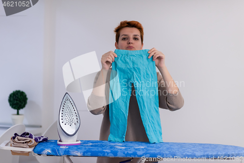 Image of Red haired woman ironing clothes at home