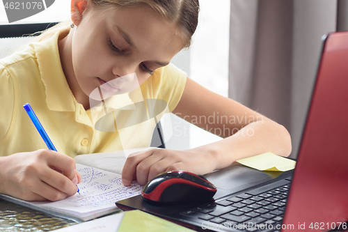 Image of Closeup of a girl who writes notes in a notebook while studying remotely