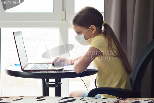Image of Girl in a medical mask watches an online lesson in a laptop