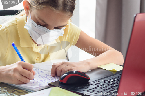 Image of Portrait of a girl in a medical mask who learns lessons sitting at a table with a computer