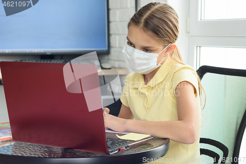 Image of A girl in a medical protective mask undergoes distance learning