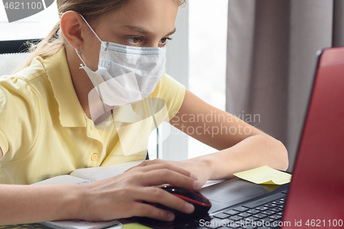 Image of Girl in medical mask is studying at the computer.