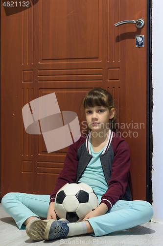 Image of A girl with a ball sits at the door and is sad