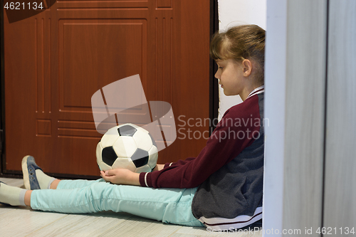 Image of The quarantined girl in self-isolation sits with a ball at the front door