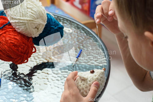 Image of The girl ties a soft toy to the mouse, sews eyes