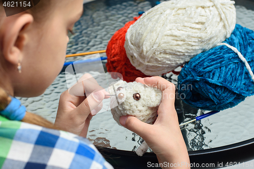 Image of Girl sews on the eyes of a homemade soft toy mouse