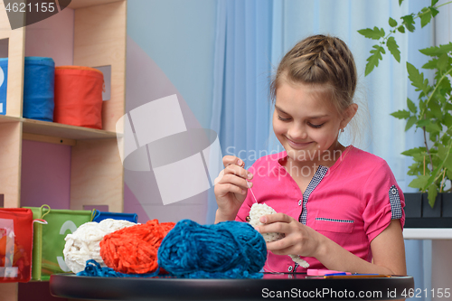 Image of Girl knits a soft toy sitting at a table in the interior of a children\'s room